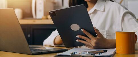 femmina studenti Nota a partire dal il libri a il asiatico ragazza biblioteca seduta a divano utilizzando il computer portatile computer e tavoletta per ricerca un in linea informazioni. nel vivente camera foto