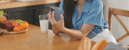 un' giovane donna con un' bellissimo viso nel un' blu camicia con lungo capelli mangiare frutta seduta dentro il cucina a casa con un' il computer portatile e taccuino per rilassamento, concetto vacanza. foto