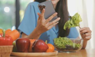 un' giovane donna con un' bellissimo viso nel un' blu camicia con lungo capelli mangiare frutta seduta dentro il cucina a casa con un' il computer portatile e taccuino per rilassamento, concetto vacanza. foto