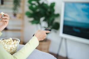 asiatico donna Guardando inteligente tv e utilizzando a distanza controllore mano Tenere televisione Audio a distanza controllo a casa con il a distanza controllo televisione foto