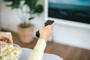 asiatico donna Guardando inteligente tv e utilizzando a distanza controllore mano Tenere televisione Audio a distanza controllo a casa con il a distanza controllo televisione foto