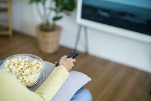 asiatico donna Guardando inteligente tv e utilizzando a distanza controllore mano Tenere televisione Audio a distanza controllo a casa con il a distanza controllo televisione foto