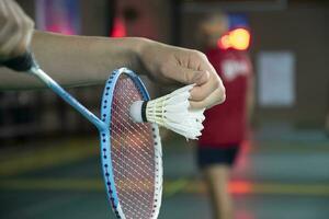 badminton giocatore detiene racchetta e bianca crema volano nel davanti di il netto prima servendo esso per un altro lato di il Tribunale foto
