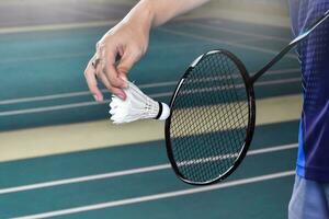 badminton giocatore detiene racchetta e bianca crema volano nel davanti di il netto prima servendo esso per un altro lato di il Tribunale foto