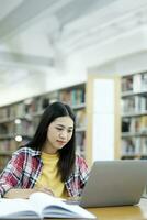 giovane Università alunno utilizzando il computer portatile per in linea apprendimento, ricerca e apprendimento a biblioteca. foto