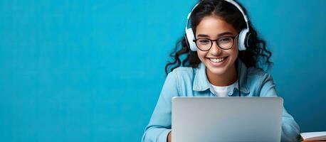 sorridente indiano adolescente ragazza utilizzando il computer portatile per in linea studia su blu sfondo contento alunno nel educativo seminario web foto