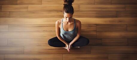 superiore giù Visualizza di un' giovane donna fare yoga in casa seduta nel un' rilassato posizione su un' di legno pavimento Meditare e scoperta interno pace la creazione di copia spazio foto