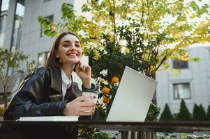 stile di vita ritratto un' allegro bella donna, libero professionista, copywriter, sviluppatore godendo caffè rompere nel estate terrazza di accogliente bar, Lavorando remoto su computer portatile, sorridente trentadue denti Sorridi guardare a telecamera foto