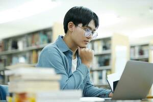 giovane Università alunno utilizzando il computer portatile per in linea apprendimento, ricerca e apprendimento a biblioteca. foto