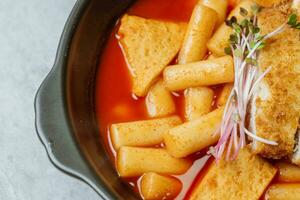 tteokbokki, un' speziato coreano piatto di Maiale cotolette, la verdura, e pesce torte servito su un' nero piatto. foto