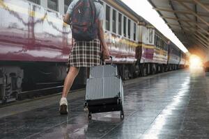 giovane femmina viaggiatore a piedi in piedi con un' valigia a treno stazione. donna viaggiatore turista a piedi in piedi sorridente con bagaglio a treno stazione foto