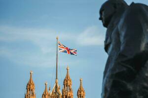 singolo unione Jack bandiera agitando nel davanti di grande Ben a il case di parlamento nel Londra, UK su un' chiaro soleggiato giorno. winston Churchill statua. foto