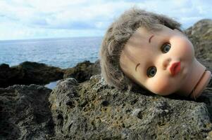 un' Bambola testa posa su il rocce di il oceano foto