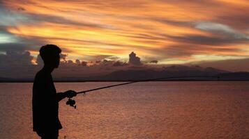 silhouette di un' pescatore con un' pesca asta nel il lago a tramonto foto