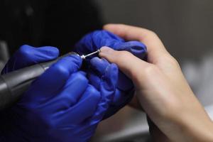 Immagine ravvicinata di manicure hardware in un salone di bellezza. manicure in guanti protettivi sta applicando un trapano elettrico per unghie per manicure sulle dita femminili.