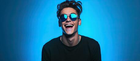 un' alla moda adolescenziale ragazzo indossare un' nero manica lunga e bicchieri pose con un' Sorridi contro un' blu sfondo illuminato di neon luci che rappresentano un' Ciao foto