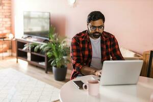 tecnologia a distanza lavoro e stile di vita concetto - contento indiano uomo nel bicchieri con il computer portatile computer Lavorando a casa ufficio, copia spazio e vuoto spazio per testo foto