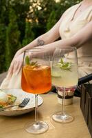 Due bicchieri di estate cocktail con ghiaccio su un' tavolo nel un' bar con un' donna nel il sfondo foto
