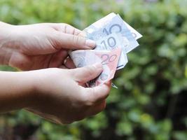 mani di una donna che conta banconote australiane in un giardino