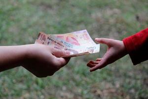 mano di una donna che consegna denaro messicano alla mano di un minore in un giardino foto