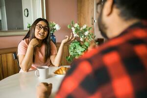 contento coppia mangiare prima colazione e parlando a cenare tavolo nel mattina. indiano ragazza e latino tipo. relazione e diversità concetto foto