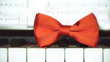 un' rosso arco cravatta si siede su superiore di un' pianoforte tastiera foto