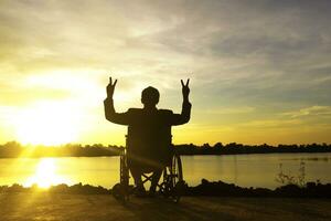 silhouette giovane Disabilitato uomo vedendo fiume sfondo.he è aumentare un' mano per e seduta su sedia a rotelle.disperazione,solitario,speranza.foto concetto depressione e paziente. foto