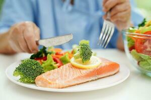 asiatico anziano donna paziente mangiare salmone palo e verdura insalata per salutare cibo nel Ospedale. foto