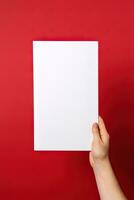 un' umano mano Tenere un' vuoto foglio di bianca carta o carta isolato su rosso sfondo. ai generato foto