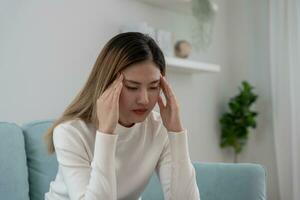 male alla testa, femmina avendo emicrania dolore, cattivo Salute, asiatico donna sensazione fatica e male alla testa, ufficio sindrome, triste stanco toccante fronte avendo emicrania o depressione, irritata ragazza, tristezza dolore foto