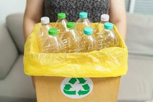 casa riciclare eco verde zero concetto donna lancio vuoto plastica bottiglia nel raccolta differenziata bidone con giallo spazzatura borse a casa. foto