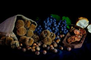 Borsa con castagne, chorizo e mazzo di uva foto