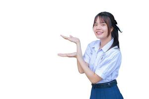 carino giovane asiatico alto scuola alunno ragazza nel scuola uniforme con sorrisi con fiducia mentre lei sembra a telecamera per presente qualcosa felicemente mentre studiando isolato su bianca foto