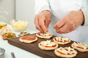 aggiungendo condimenti per il mini pizze. aggiungendo formaggio. delizioso fatti in casa mini pizze preparazione. foto