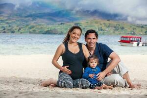 giovane coppia in attesa per loro secondo bambino avendo divertimento con loro bambino ragazza a il bellissimo bianca spiaggia di lago tota collocato nel il Dipartimento di boyaca a 3.015 metri sopra mare livello nel Colombia foto