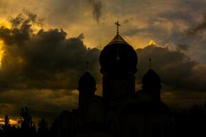 il silhouette di il cupole di un ortodosso cristiano Chiesa nel Romania contro il sfondo di il rosso cielo. fede o religione concetto foto