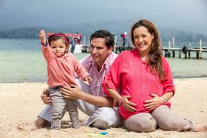 giovane coppia in attesa per loro secondo bambino avendo divertimento con loro bambino ragazza a il bellissimo bianca spiaggia di lago tota collocato nel il Dipartimento di boyaca a 3.015 metri sopra mare livello nel Colombia foto