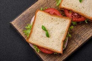 delizioso Sandwich con pane abbrustolito, prosciutto, pomodori, formaggio e lattuga foto