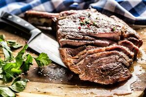 appena grigliato tomahawk bistecca su ardesia piatto con sale Pepe rosmarino e prezzemolo erbe aromatiche. affettato pezzi di succoso Manzo bistecca foto