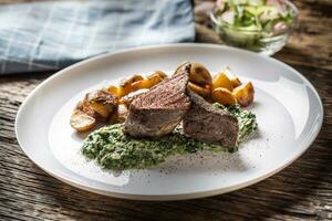 delizioso grigliato Manzo sous vedasi bistecca servito su un' bianca piatto con croccante arrostito patate, spinaci tuffo e fresco foglia lattuga insalata foto