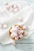 superiore ritratto Visualizza di un' di legno ciotola pieno di rosa e bianca marshmallows con alcuni sparpagliato in giro su un' bianca tavolo stoffa foto