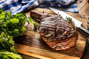 appena grigliato tomahawk bistecca su ardesia piatto con sale Pepe rosmarino e prezzemolo erbe aromatiche foto