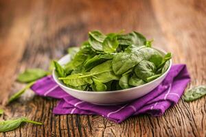spinaci. fresco bambino spinaci le foglie nel piatto su woden tavolo foto