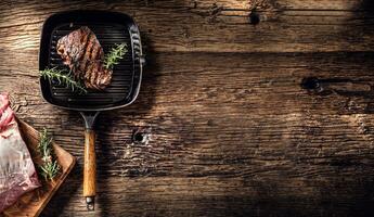 grigliato Manzo bistecca nel griglia padella con erbe aromatiche rosmarino su di legno tavolo foto