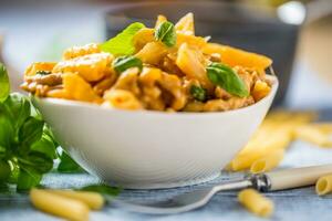 pasta penne con pollo pezzi funghi basilico e parmigiano formaggio italiano cibo nel bianca ciotola su cucina tavolo foto