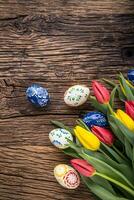 Pasqua. mano fatto Pasqua uova e primavera tulipani su vecchio di legno tavolo. foto