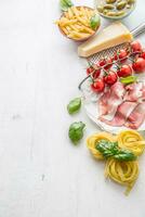 italiano o mediterraneo cibo cucina e ingredienti su bianca calcestruzzo tavolo. tagliatelle pene pasta olive oliva olio pomodori parmigiano formaggio prosciutto e basilico le foglie su bianca calcestruzzo tavola foto