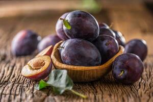 prugne. fresco succoso prugne nel un' ciotola su un' di legno o calcestruzzo tavola foto