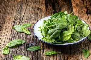 spinaci. fresco bambino spinaci le foglie nel piatto su woden tavolo foto