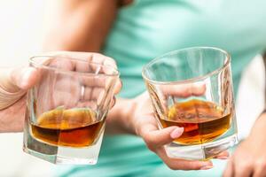 uomo e donna mani tostatura con bicchieri di whisky Brandy o Rum in casa - avvicinamento foto